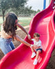 Mom with brown hair and white Apollo wearable on right wrist helping 3 year old son slide down red slide in an outdoor park