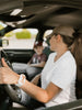 Women driving car with white shirt and brown hat with Apollo wearable on wrist with young son in car.