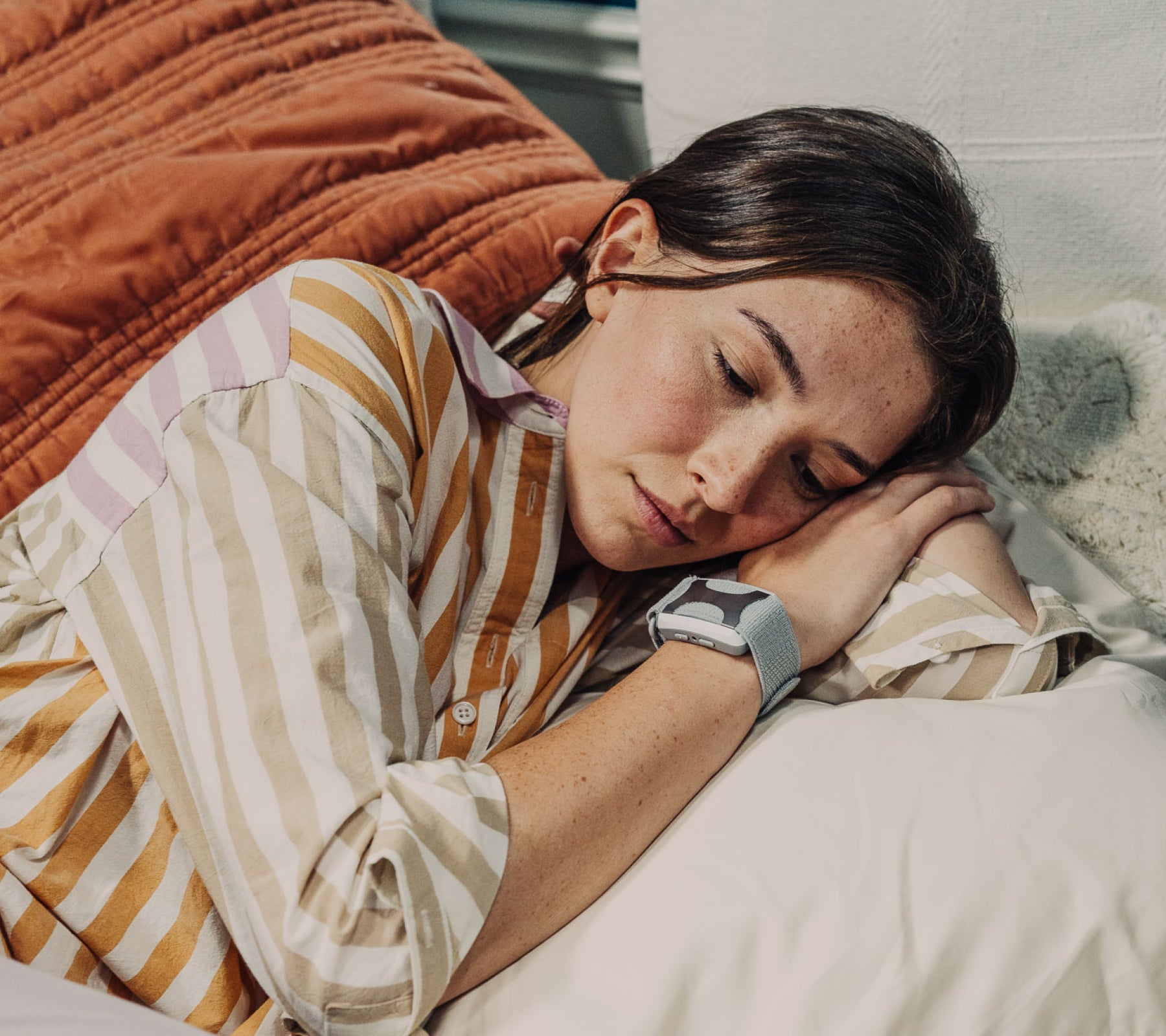 Brunette women sleeping on her side in striped pajamas with a white Apollo wearable.
