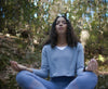Woman meditating in the forest in lotus pose with an Apollo on her wrist
