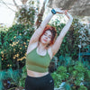 Women with red hair and green tank top and black leggings in front of garden background stretching her arms up with the Apollo wearable on her wrist