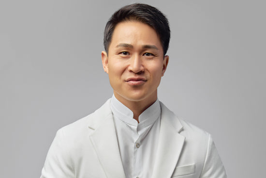 Dr. Halland Chen in a white suit jacket in front of a grey background