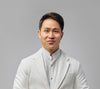 Dr. Halland Chen in a white suit jacket in front of a grey background