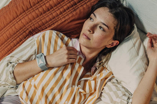 Women in striped shirt laying in bed with an Apollo wearable on her right wrist