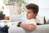 10 year old boy on a grey couch looking to the left of the camera over his should with an Apollo wearable on his wrist