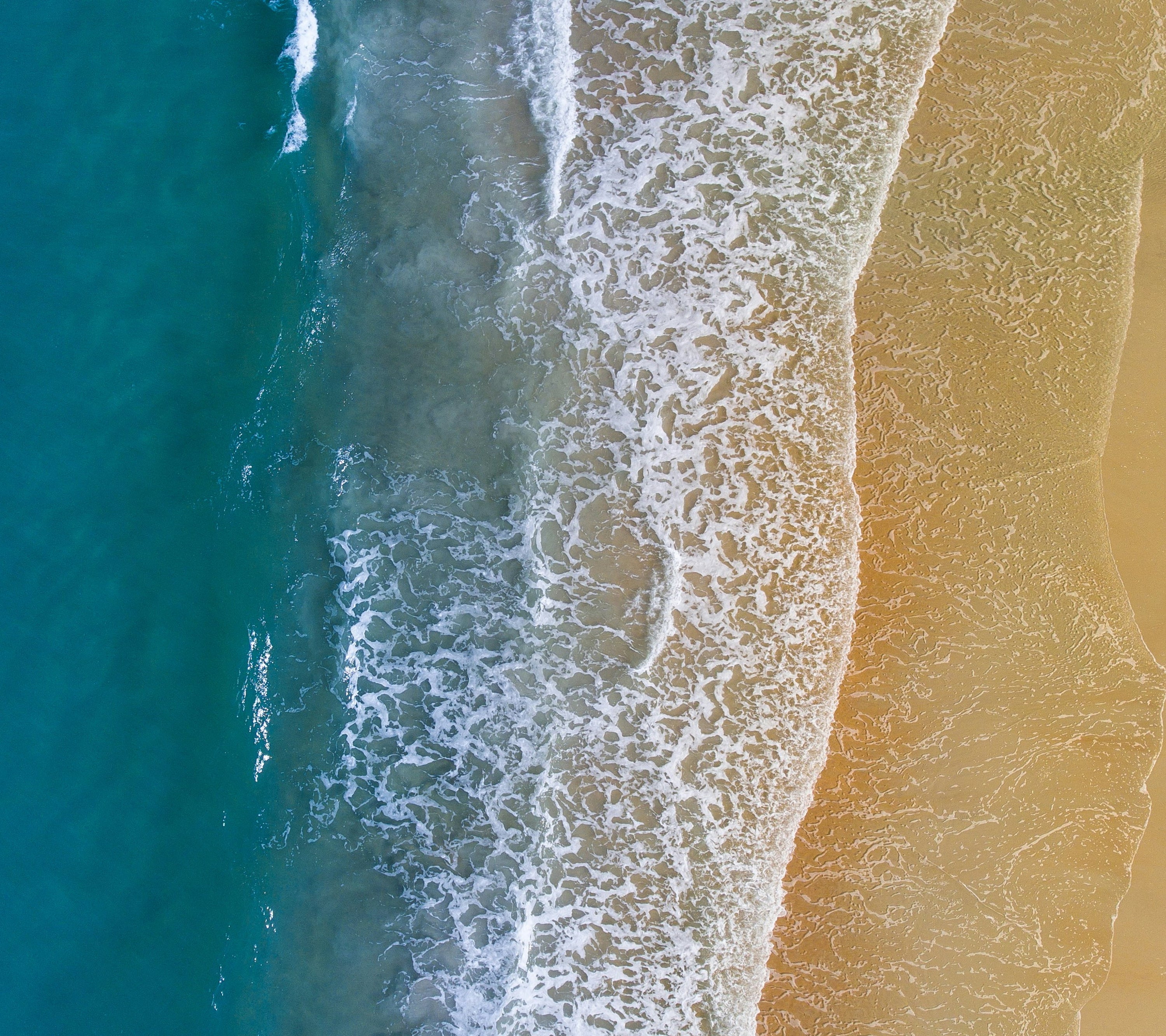 Aerial view of a wave crashing on the beach.