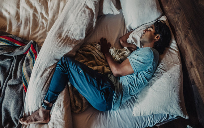 Man wearing blue pajamas asleep on his right side with an Apollo wearable on his left ankle