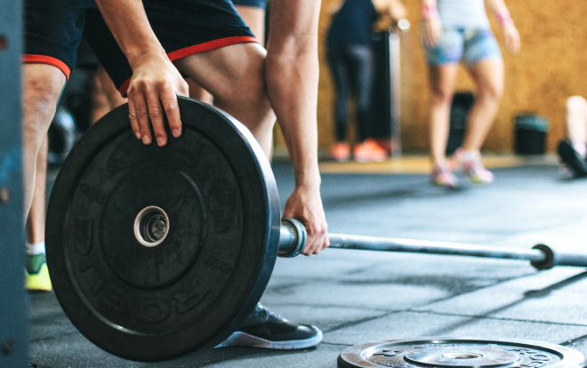 Man with black shorts and sneakers setting up weight in a gym setting.