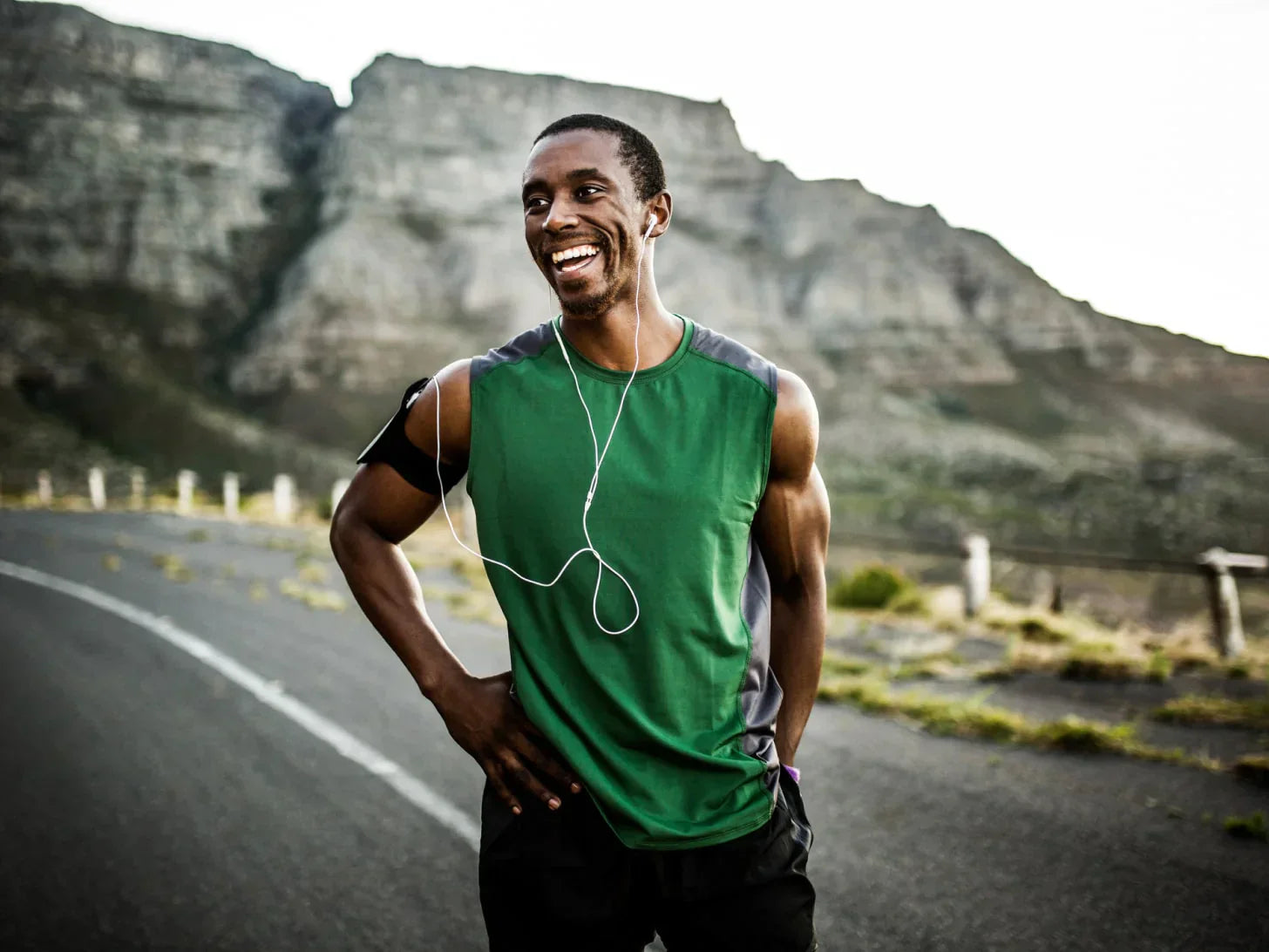 Man running on a road with a cliff behind him in green tank top.