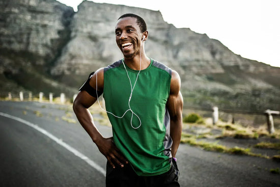 Man running on a road with a cliff behind him in green tank top.