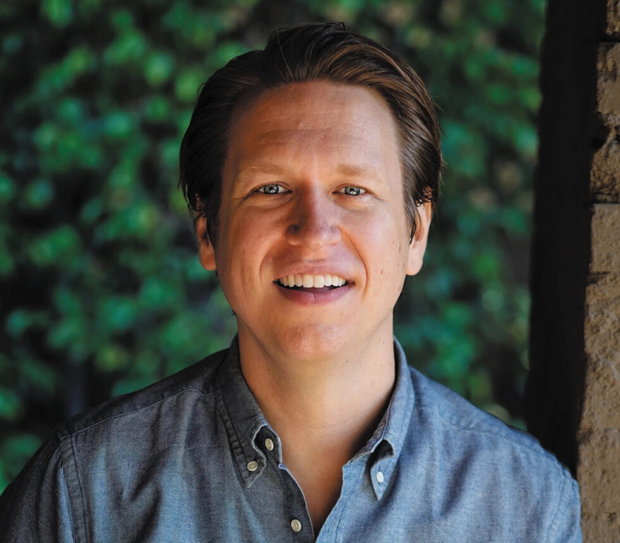 Man smiling outdoors with greenery in the background